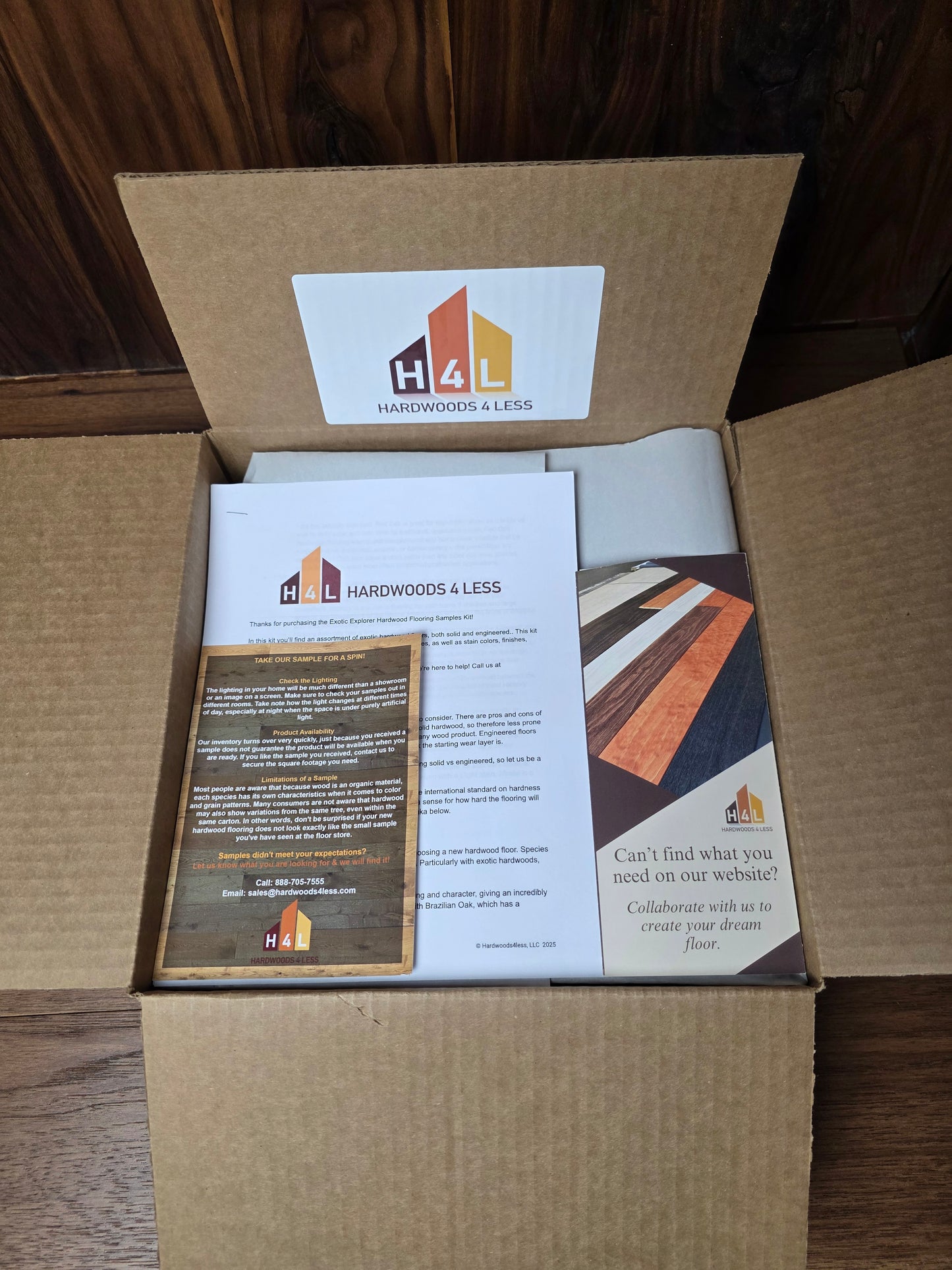 Open cardboard box with printed materials and a hardwoods4less logo on a wooden surface