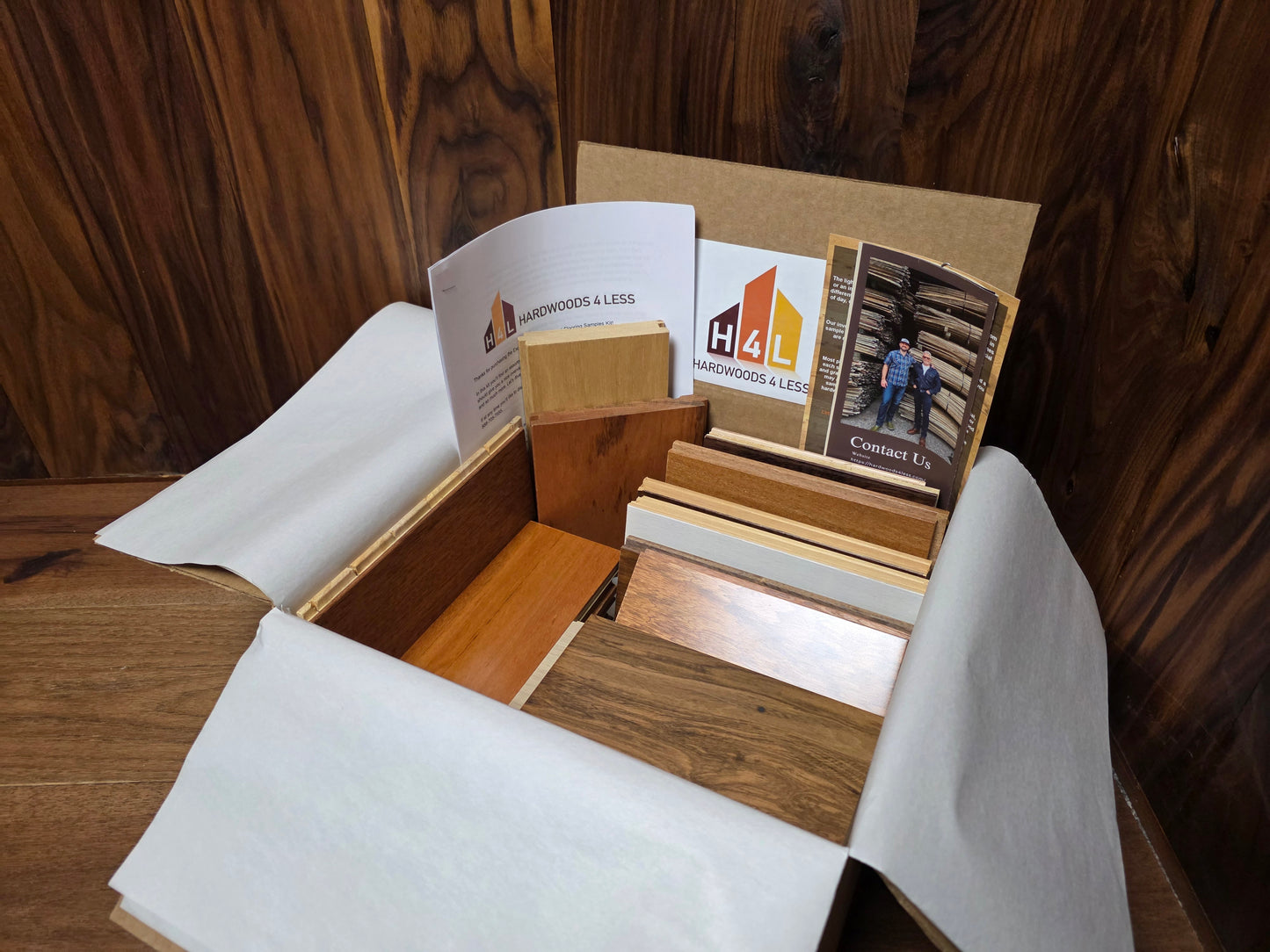 Open box containing Hardwood Flooring Samples and a brochure with 'H4L' branding on a wooden surface.