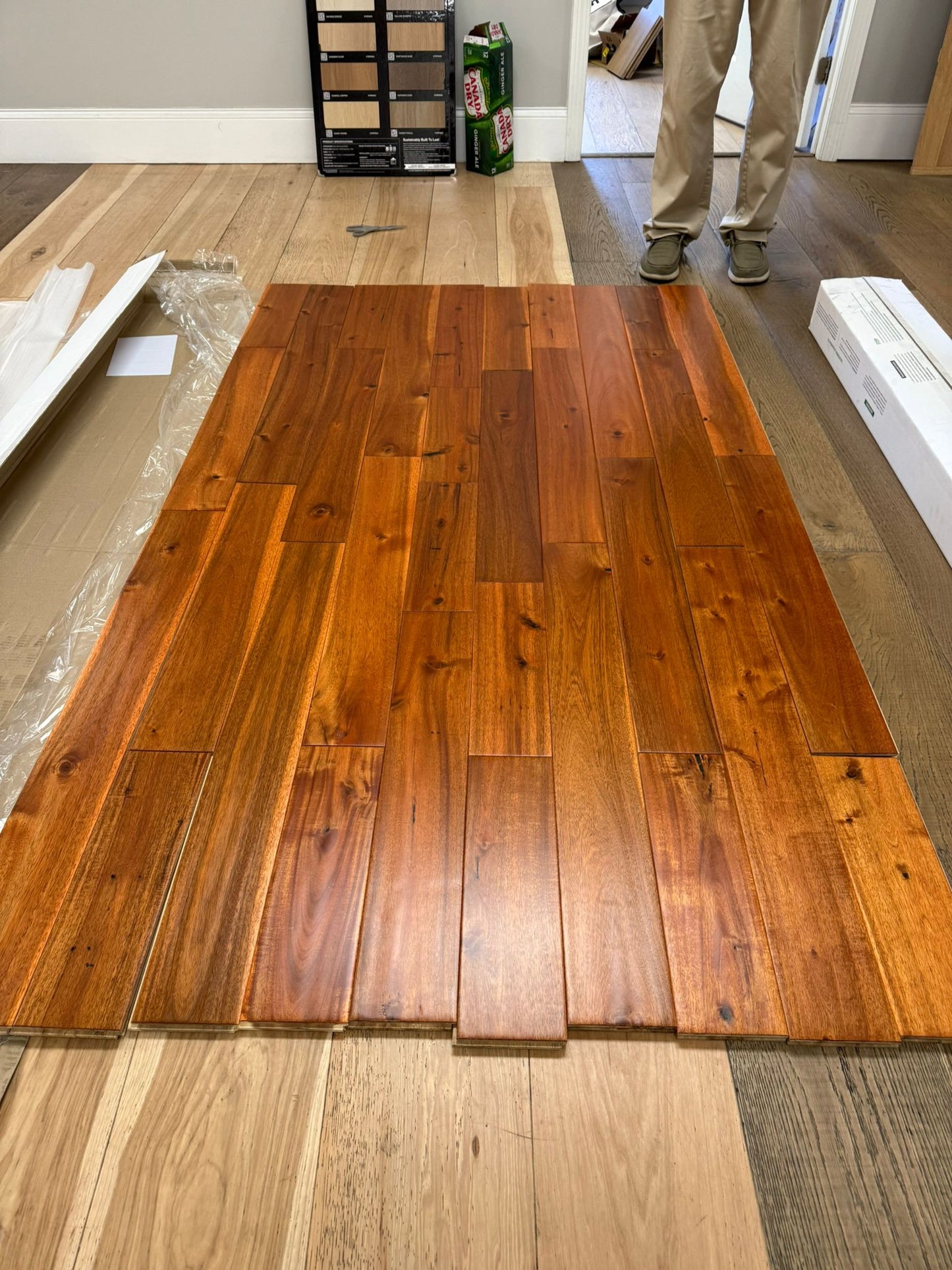 5" x 3/4" Solid Acacia Golden Hour Hardwood Flooring. Shown on a floor as a whole box. A person stands to the back right. 