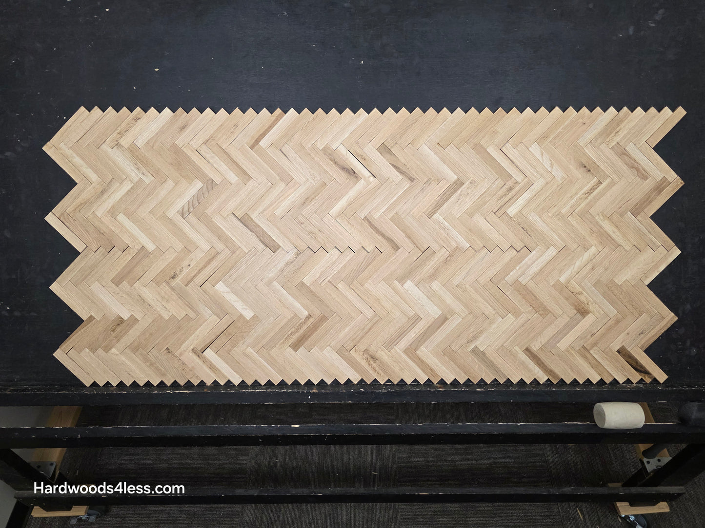 14 1/8" x 18 1/8" x 5/16" Unfinished White Oak Herringbone Parquet Flooring. 6 tiles wide on a black shooting table.