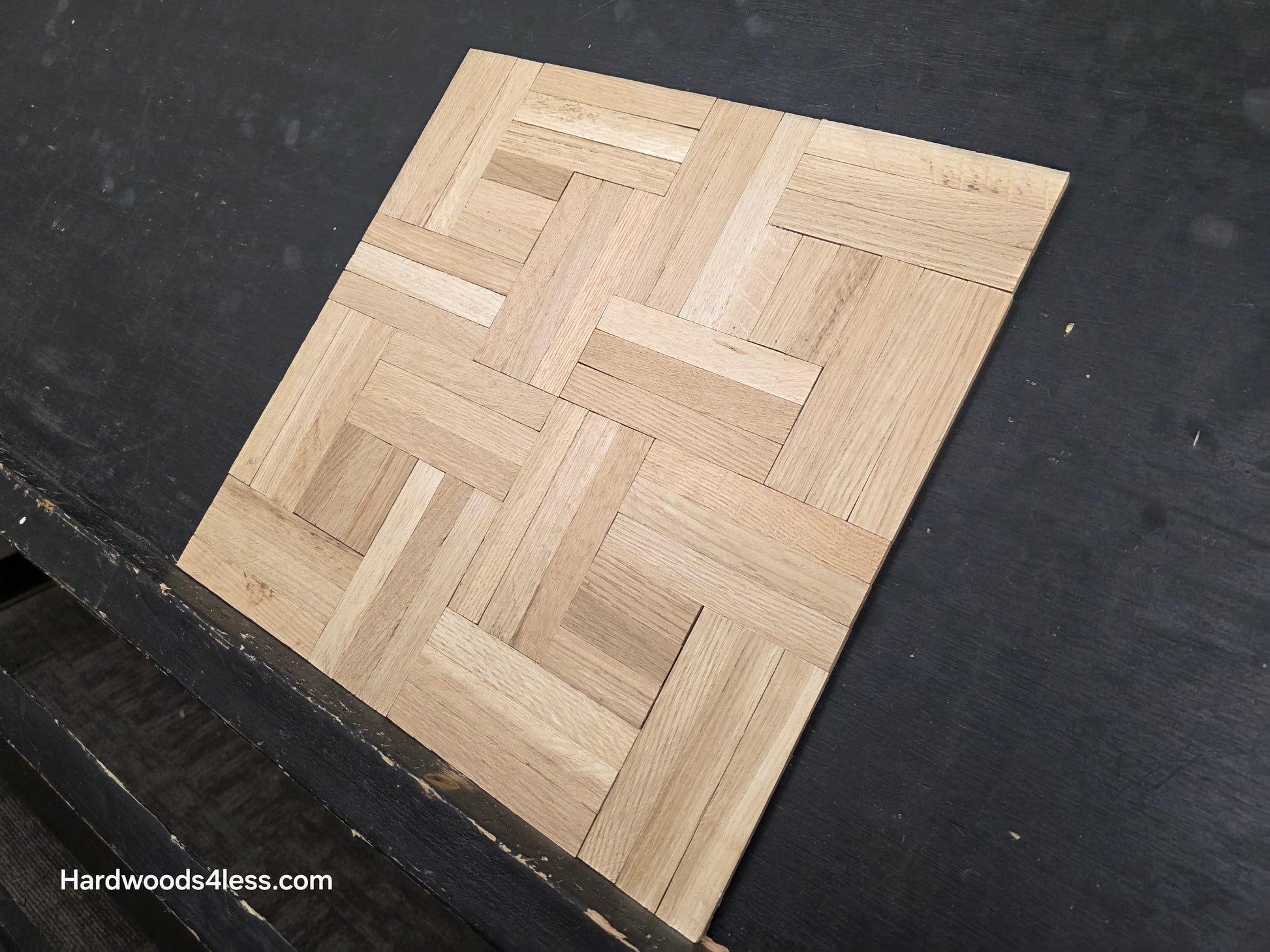 14 ¼ x 14 ¼ x 5/16 Unfinished White Oak Haddon Hall Parquet Flooring. Shown on a black shooting table. steep right hand close up. 