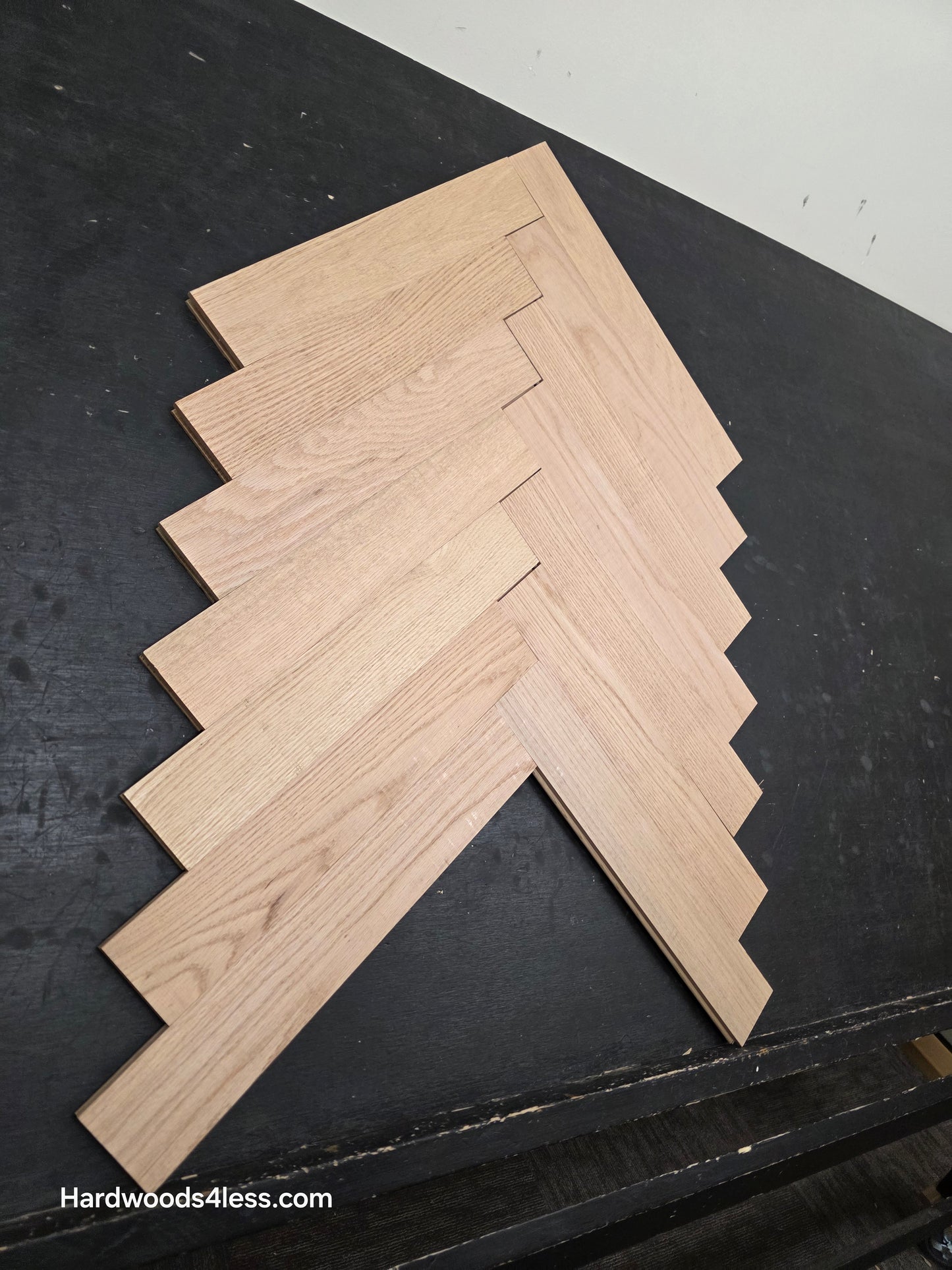 3 14 x 19 12 x 34 Solid Unfinished Red Oak Herringbone Hardwood Flooring. Shown on a black shooting table. Shot from steep left.