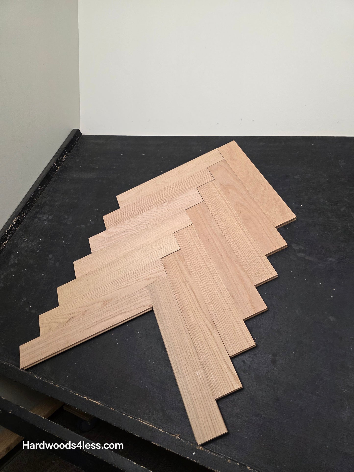 3 14 x 19 12 x 34 Solid Unfinished Red Oak Herringbone Hardwood Flooring. Shown on a black shooting table. Shot from wide right.
