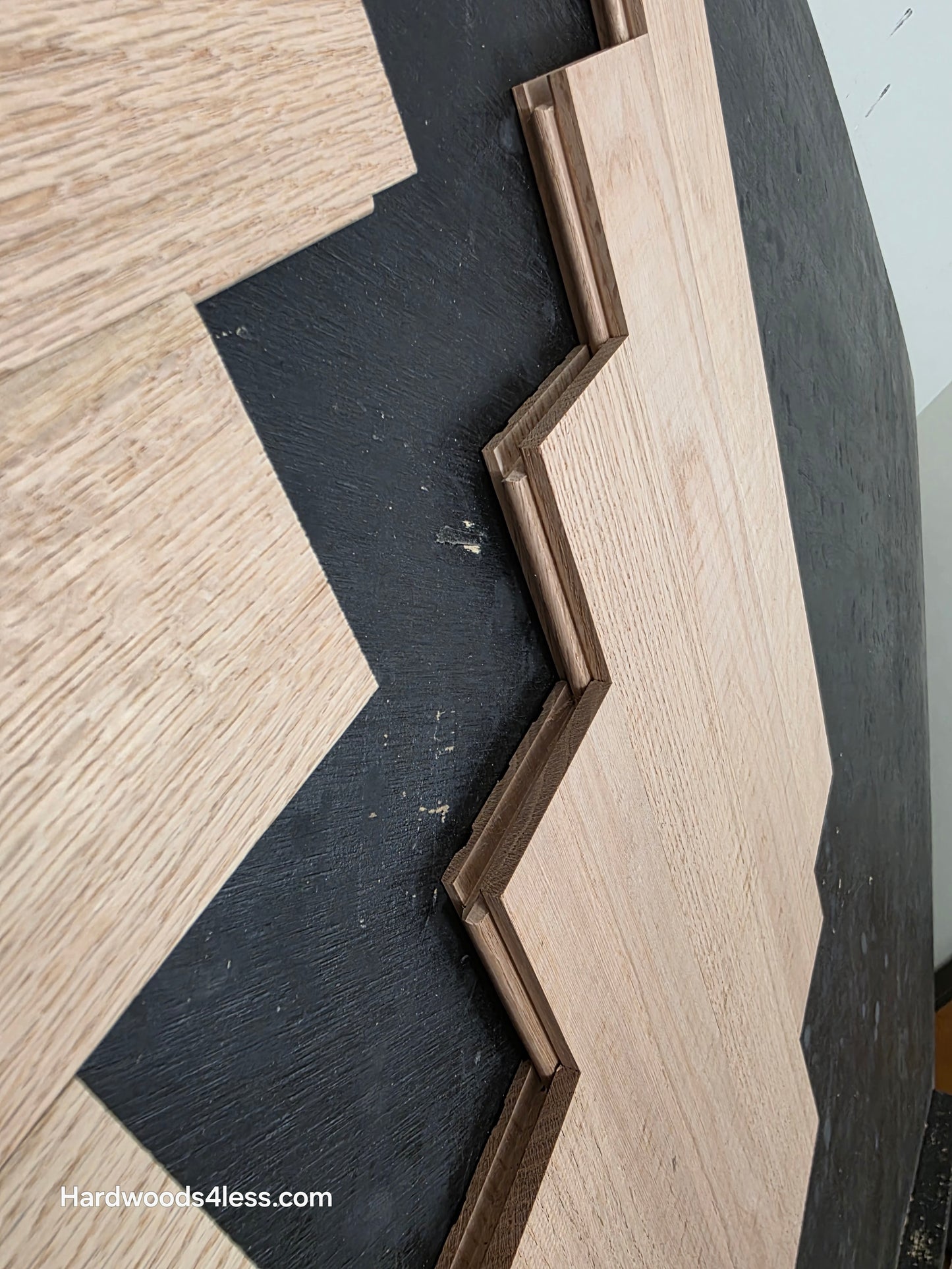 3 14 x 19 12 x 34 Solid Unfinished Red Oak Herringbone Hardwood Flooring. Shown on a black shooting table. Close up of the grooves.