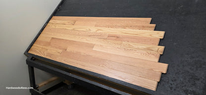 3 1/4" x 3/4" Red Oak Natural Common & Better Low Gloss Hardwood Flooring. shown on a black shooting table. Shot from wide right. 