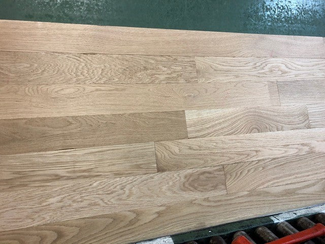 4 x 3/4 Unfinished White Oak Select & Better Solid Hardwood Flooring on a green shooting rack with black rollers. head on shot