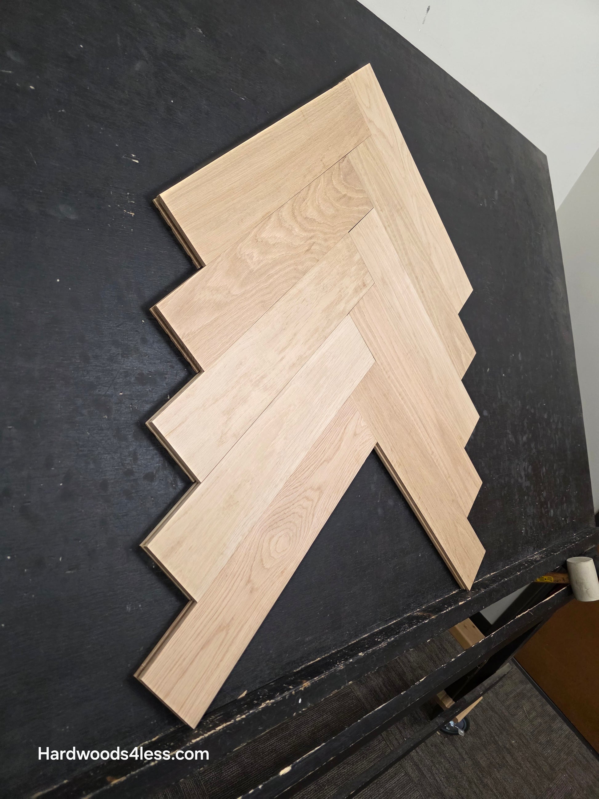 4" x 20" x 3/4" Solid Unfinished White Oak Herringbone Hardwood Flooring. Shown on a black shooting table. Shot from low left.