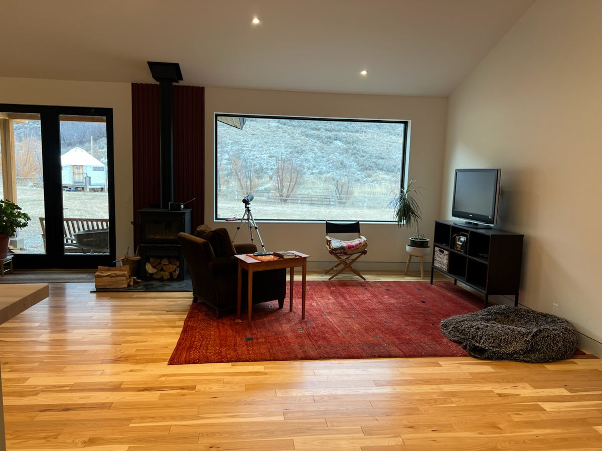 4 x 34 American Hickory Natural Hardwood Flooring. shown in a living room. There is a big window at center with a red rug in the middle of the room. Some furniture sits around the rug.