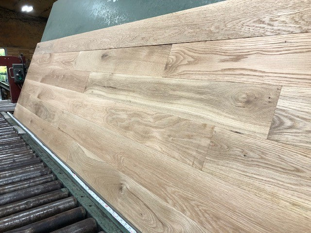 5" x 3/4" Unfinished White Oak #1 Common Solid Hardwood Flooring shown on a green shooting table with rollers at the base 
