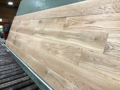 5" x 3/4" Unfinished White Oak #1 Common Solid Hardwood Flooring shown on a green shooting table with rollers at the base 