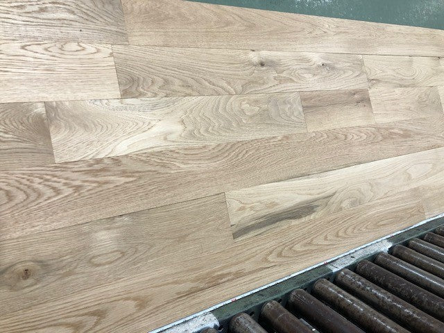 5" x 3/4" Unfinished White Oak #1 Common Solid Hardwood Flooring shown on a green shooting table with rollers at the base 