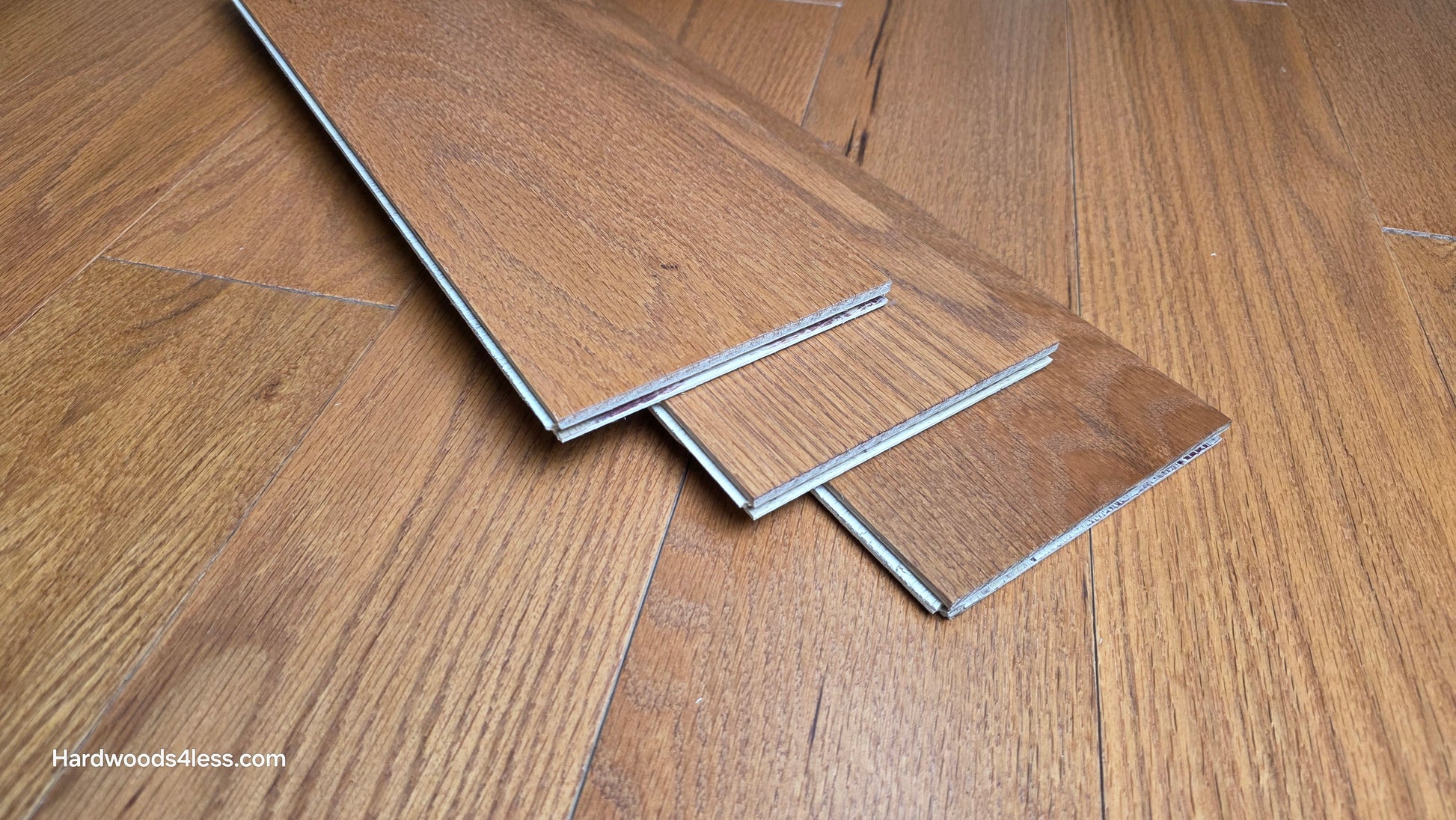 5" x 1/2" Engineered Red Oak Golden Oak Hardwood Flooring. Three wood flooring planks are shown at center. The planks are sitting on top of the Golden Oak flooring. 