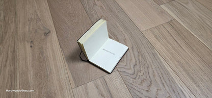 6 1/2" x 1/2" Engineered European White Oak Mojito Hardwood Flooring. Shown with an open small book with the words, Hardwoods4less, written in the center. 