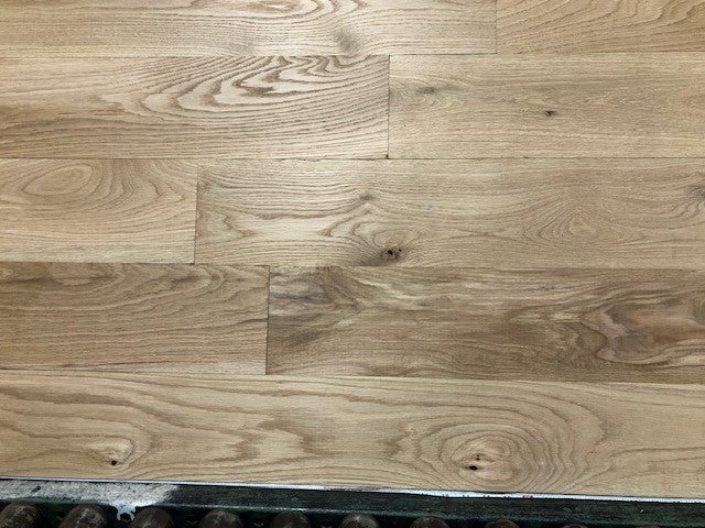 6" x 3/4" Unfinished White Oak #1 Common Solid Hardwood Flooring on a green shooting rack. Rollers can be seen at the base.