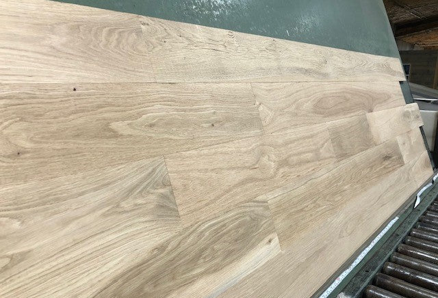 6" x 3/4" Unfinished White Oak #1 Common Solid Hardwood Flooring on a green shooting rack. Rollers can be seen at the base.