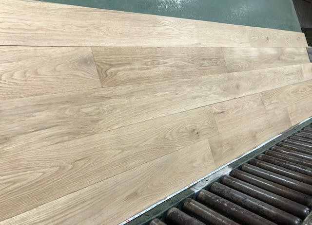 6" x 3/4" Unfinished White Oak #1 Common Solid Hardwood Flooring on a green shooting rack. Rollers can be seen at the base.