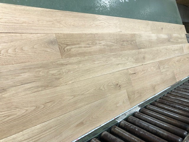 6" x 3/4" Unfinished White Oak #1 Common Solid Hardwood Flooring on a green shooting rack. Rollers can be seen at the base.
