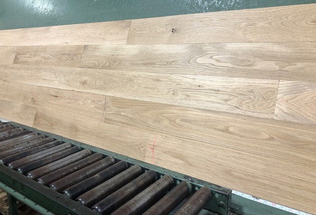 6" x 3/4" Unfinished White Oak #1 Common Solid Hardwood Flooring on a green shooting rack. Rollers can be seen at the base.