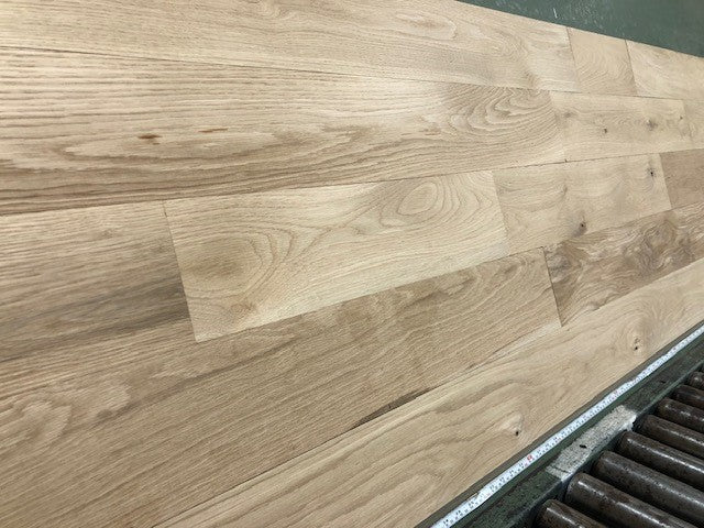 6" x 3/4" Unfinished White Oak #1 Common Solid Hardwood Flooring on a green shooting rack. Rollers can be seen at the base.