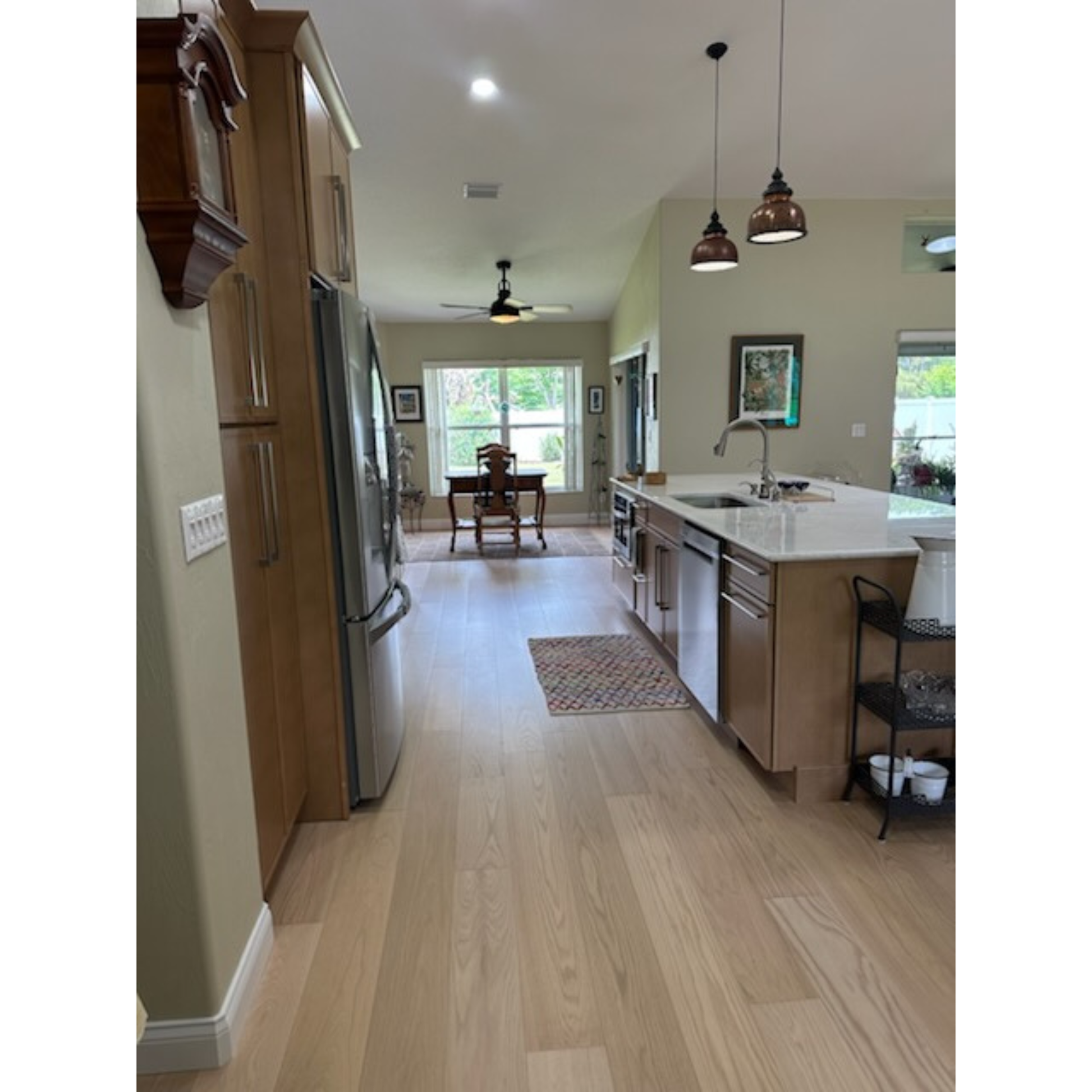7 x 58 Engineered Red Oak Hudson Hardwood Flooring installed in kitchen. On the right is a wooden island with a marble top and sink. To left is a fridge and more wooden accents. 
